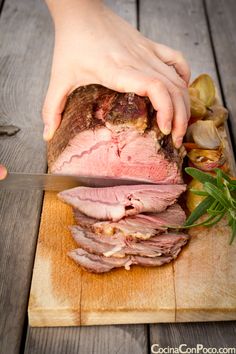 a person slicing meat on top of a wooden cutting board