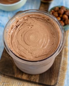 a bowl filled with chocolate frosting next to nuts on a wooden board and blue table cloth