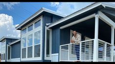 a man standing on top of a balcony next to two blue houses with white balconies