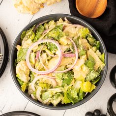 a salad with onions and lettuce in a black bowl next to other food items