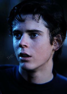 a young man with dark hair and blue eyes looking at the camera, wearing a black t - shirt