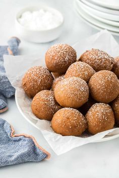 a white bowl filled with sugar covered donuts on top of a table next to plates and napkins