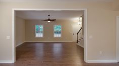 an empty living room with hard wood floors and ceiling fan in the corner, looking into the dining area