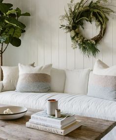 a white couch sitting next to a wooden table with books on it and a wreath hanging above the couch