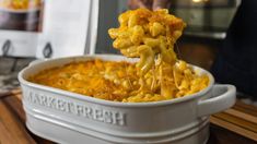 a person scooping out some macaroni and cheese from a casserole dish