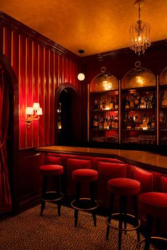 a dimly lit bar with red leather stools and chandelier hanging from the ceiling