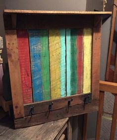 an old wooden box is painted with multicolored paint and has hooks on it