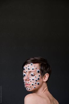 a shirtless man with black dots painted on his face and chest by an unknown object in the background