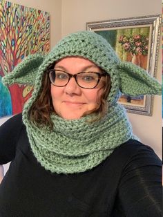 a woman wearing a knitted yoda hat and scarf in front of some paintings