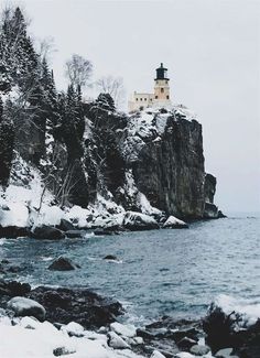 a light house sitting on top of a cliff next to the ocean covered in snow