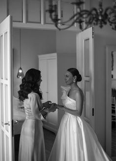 two women in dresses are standing near each other and one is looking at the mirror