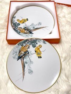 two plates with birds painted on them sitting in a box next to a white furnishing