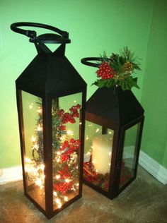 two black lanterns with christmas decorations on them, one is lit and the other is decorated