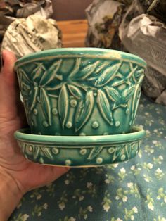 a hand holding two green bowls on top of a blue cloth covered table with other items in the background