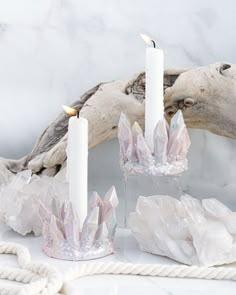 two white candles sitting on top of a table next to some driftwood and rope