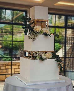 a three - tiered white wedding cake with flowers on top and greenery around the edges