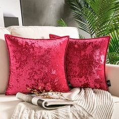 two red pillows sitting on top of a white couch next to a potted plant