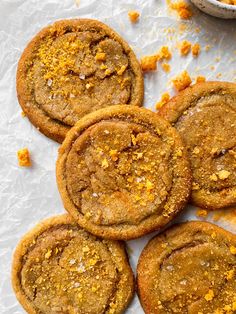 several cookies with orange zest are on the table next to a bowl of crumbs