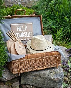 a wicker suitcase filled with hats sitting on top of a pile of rocks next to a sign that says help yourself