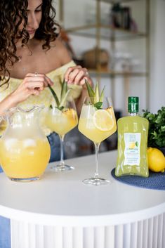 a woman sitting at a table with two glasses filled with lemonade and a pineapple