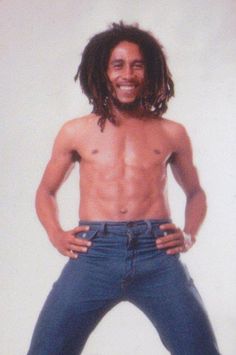 a man with dreadlocks standing in front of a white wall and smiling at the camera