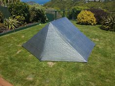 a tent pitched up in the grass on top of a hill with ocean and mountains in the background