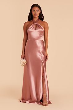 a woman wearing a pink satin gown with an open neck and high slits, standing in