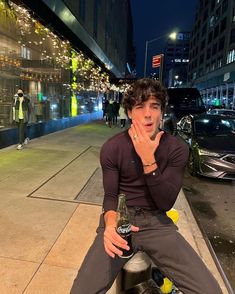 a young man sitting on top of a fire hydrant holding a beer in his hand