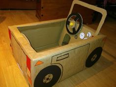 a cardboard box shaped like a car with wheels and steering wheel on the inside, sitting on a wooden floor