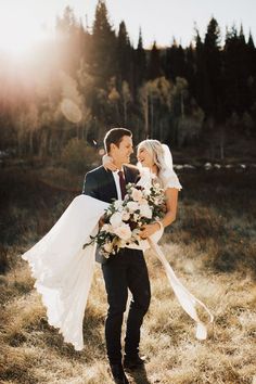 a bride and groom are walking through the grass holding each other in their arms while they smile