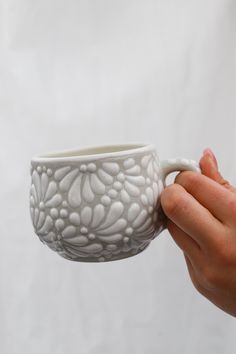 a hand holding a white ceramic cup in front of a white background