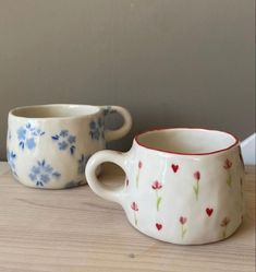 two coffee cups sitting next to each other on top of a wooden table, one with blue and red flowers painted on it