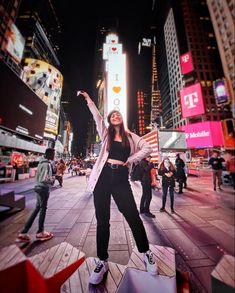 a woman standing in the middle of a busy city at night with her arms up