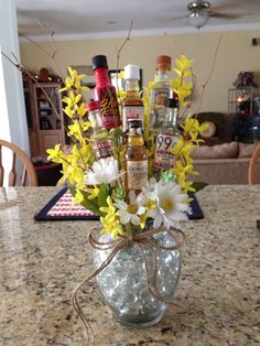 a vase filled with liquor bottles and flowers on top of a kitchen counter next to a dining room table