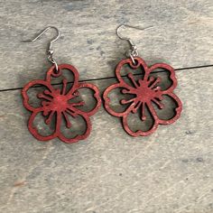 two red flower shaped metal earrings sitting on top of a wooden table