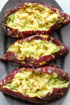 three stuffed red potatoes with avocado and cheese on top, sitting on a gray plate