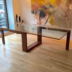 a glass table sitting on top of a hard wood floor next to a large painting