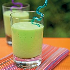 two glasses filled with green liquid sitting on top of a colorful table cloth next to each other