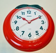 a red clock with green hands and numbers on it's face sits on a white surface