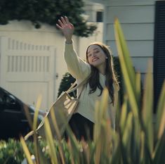 a woman is waving to the sky while standing in front of a house with her hand up