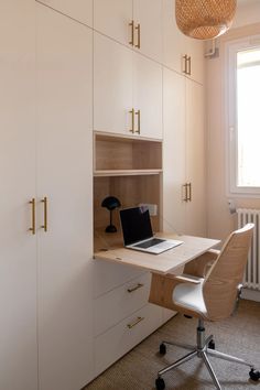 a desk with a laptop on it in front of a white cupboards and window