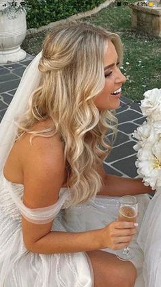 a woman in a wedding dress sitting on the ground holding a wine glass and flowers