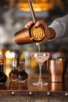 a bartender is pouring a drink into a wine glass with two liquor bottles in the background