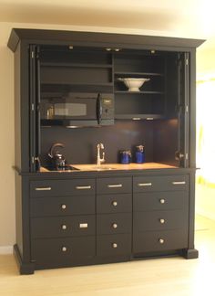 a kitchen with black cabinets and wooden counter tops in front of a microwave oven on top of a cabinet