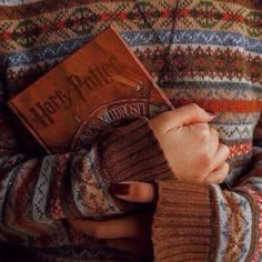 a person is holding a book in their hands and wearing a sweater with an interesting pattern on it