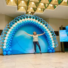 a woman standing in front of a blue and white arch with balloons on it's sides