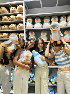 four girls are holding stuffed animals in front of shelves full of stuffed penguin heads and hats