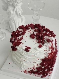 a white cake decorated with red flowers and angel figurine next to it on a table