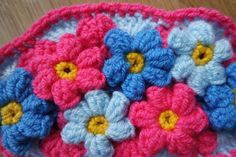 crocheted flowers are displayed in a pink, blue and white dishcloth on a wooden surface