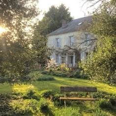 a bench sitting in front of a large house with lots of trees and bushes around it